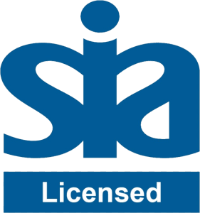 A professional male security operator in a UK control room monitoring high-definition surveillance screens with his SIA license badge displayed.