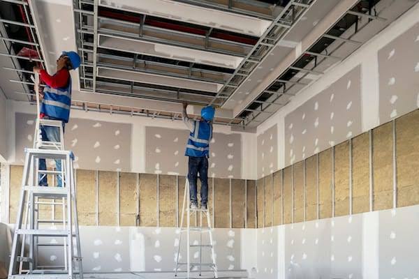 A professional installer mounting plasterboard on a metal frame to earn a dry lining fixing qualification.