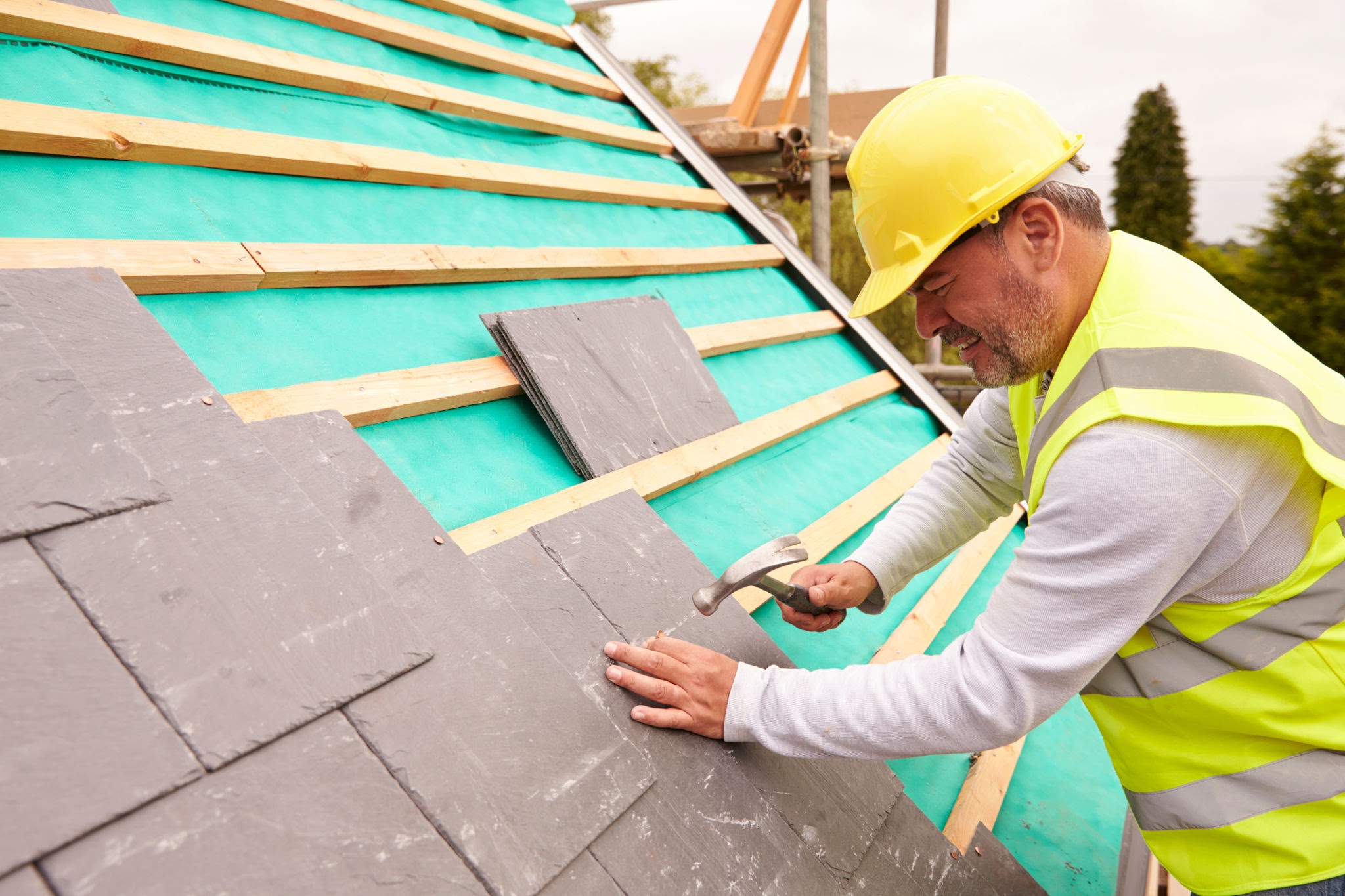 A professional roofer fixing natural slates to timber battens on-site for his roofing occupations NVQ portfolio.